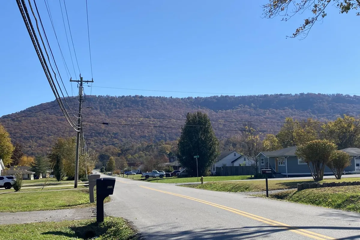 A peaceful view of a neighborhood street with a clear, majestic mountain in the background. The scene includes a mailbox in the foreground and neighboring houses, evoking a tranquil community feel and direct connection to natural scenery.