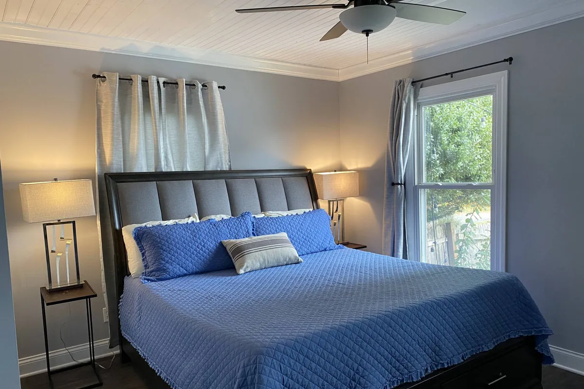 A peaceful bedroom scene with a bed covered by a soft blue quilt, side lamps, and a window letting in gentle natural light. The atmosphere is one of tranquility, perfect for reading or enjoying a restful night's sleep.