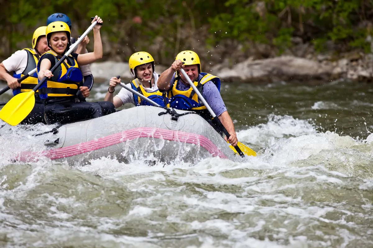 A group of adventurers navigate a white-water rafting boat, paddling through lively river water surrounded by lush greenery. The image captures the excitement and camaraderie of outdoor adventure.