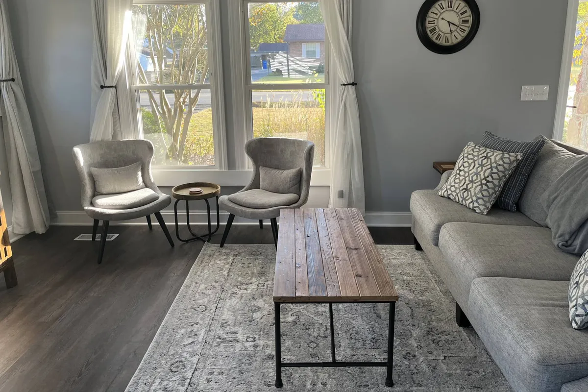 A bright and inviting living area featuring a comfortable seating arrangement, a rustic coffee table, and expansive windows that fill the room with natural light. The space exudes both functionality and warmth, offering an ideal spot for relaxation or small gatherings.