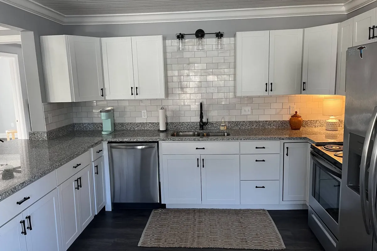 A stylish, modern kitchen with granite countertops, a modern sink, stainless steel appliances, and a subway tile backsplash. Details like the coffee maker and clean lines evoke a sense of convenience and readiness for culinary adventures.