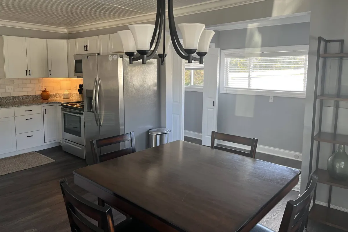 A comfortable dining area adjacent to the kitchen, featuring a dining table with seating for four, modern appliances in view, and a large window letting in natural light. The arrangement invites shared meals and easy conversation, underscoring the family-friendly atmosphere.